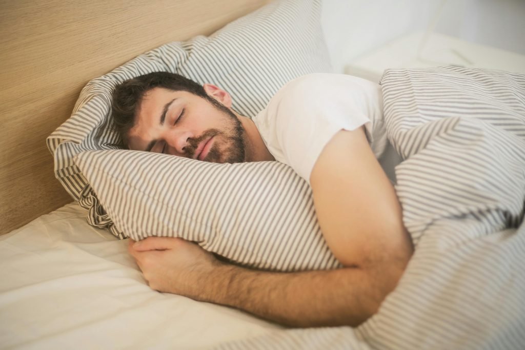 Man in deep sleep hugging a pillow, representing restful sleep and proper sleep posture for better recovery
