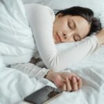 Woman sleeping peacefully in white bedding, demonstrating healthy sleep habits and optimal sleep environment